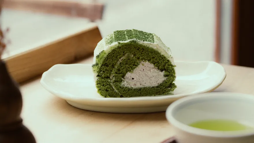 A slice of green tea sponge roll cake with cream inside