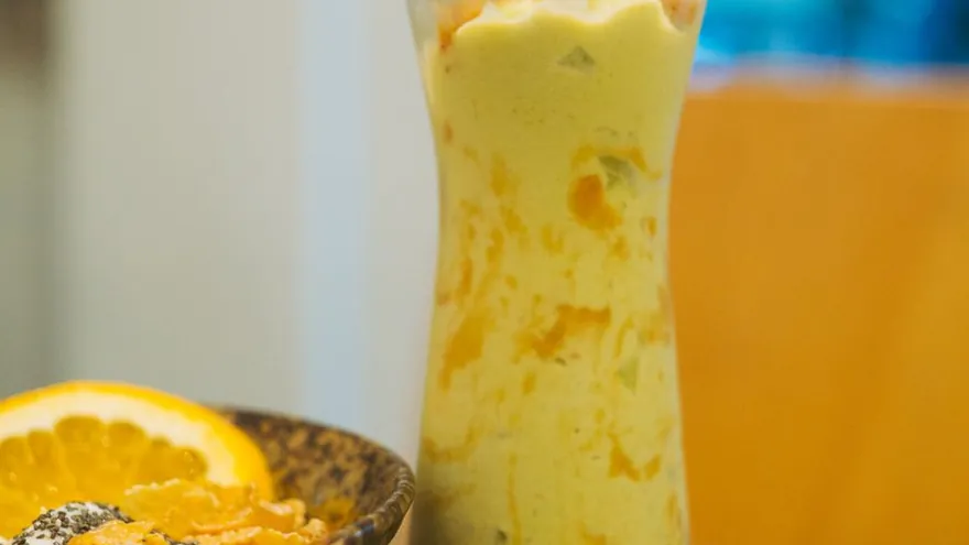 A tall glass of yellow mango drink with ice